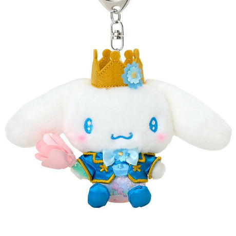 Sanrio Cinnamoroll plush keychain dressed as a prince in a blue and gold royal suit with a matching crown, holding a pink fabric tulip, attached to a silver metal lobster clasp.