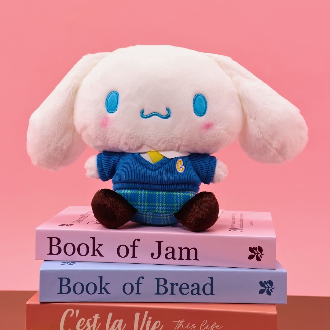 Sanrio officially licensed Cinnamoroll plush doll dressed in a school uniform. He wears a blue plaid skirt, a V-neck blue sweater, a yellow tie, and is seated on a stack of books with colorful spines. The soft, white plush features Cinnamoroll's iconic blue-embroidered eyes and swirling mouth, making it a perfect collectible toy.