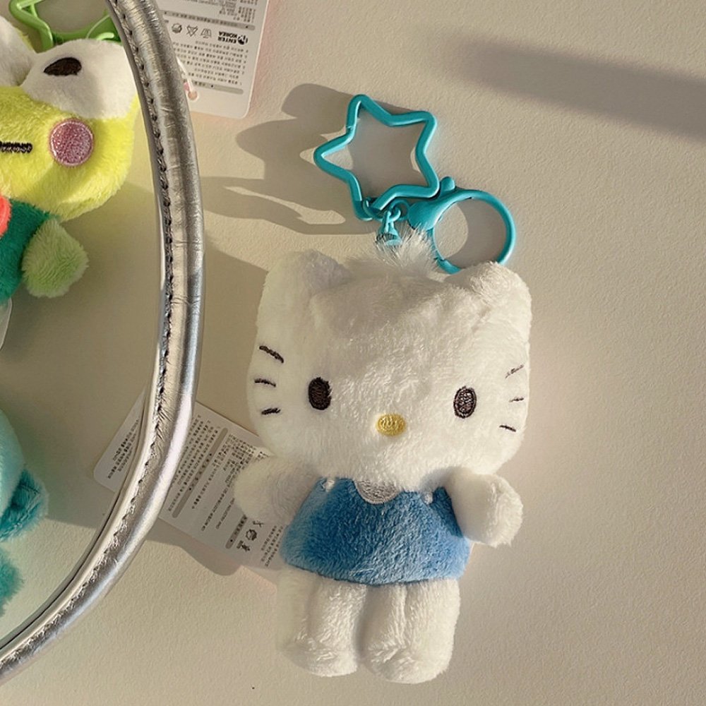 White Dear Daniel plush toy with blue dress attached to a turquoise star-shaped keychain on a beige surface.