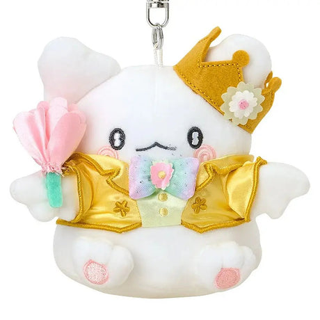 A plush keychain of the Sanrio character Hanamaruobake, a white bear with pink blush on his cheeks. He is wearing a golden crown with a white flower, a shiny yellow tuxedo jacket with gold trim, and a pastel rainbow bowtie. He holds a soft pink flower in his hand and is attached to a silver metal lobster clasp.