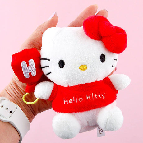 Plush toy Hello Kitty with a red bow held by a hand against a pink background