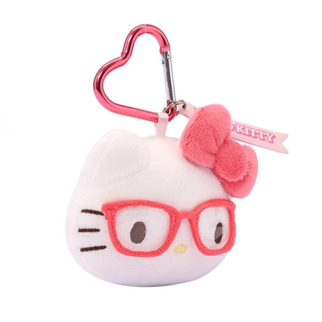 An officially licensed Sanrio Hello Kitty plush head keychain,  wearing embroidered pink glasses and a textured pink bow. The keychain features a pink, heart-shaped metal carabiner clip and a woven fabric tag that reads "HELLO KITTY." The sturdy, heart-shaped carabiner in a matching metallic pink finish, makes it easy to clip onto backpacks, purses, or belt loops.