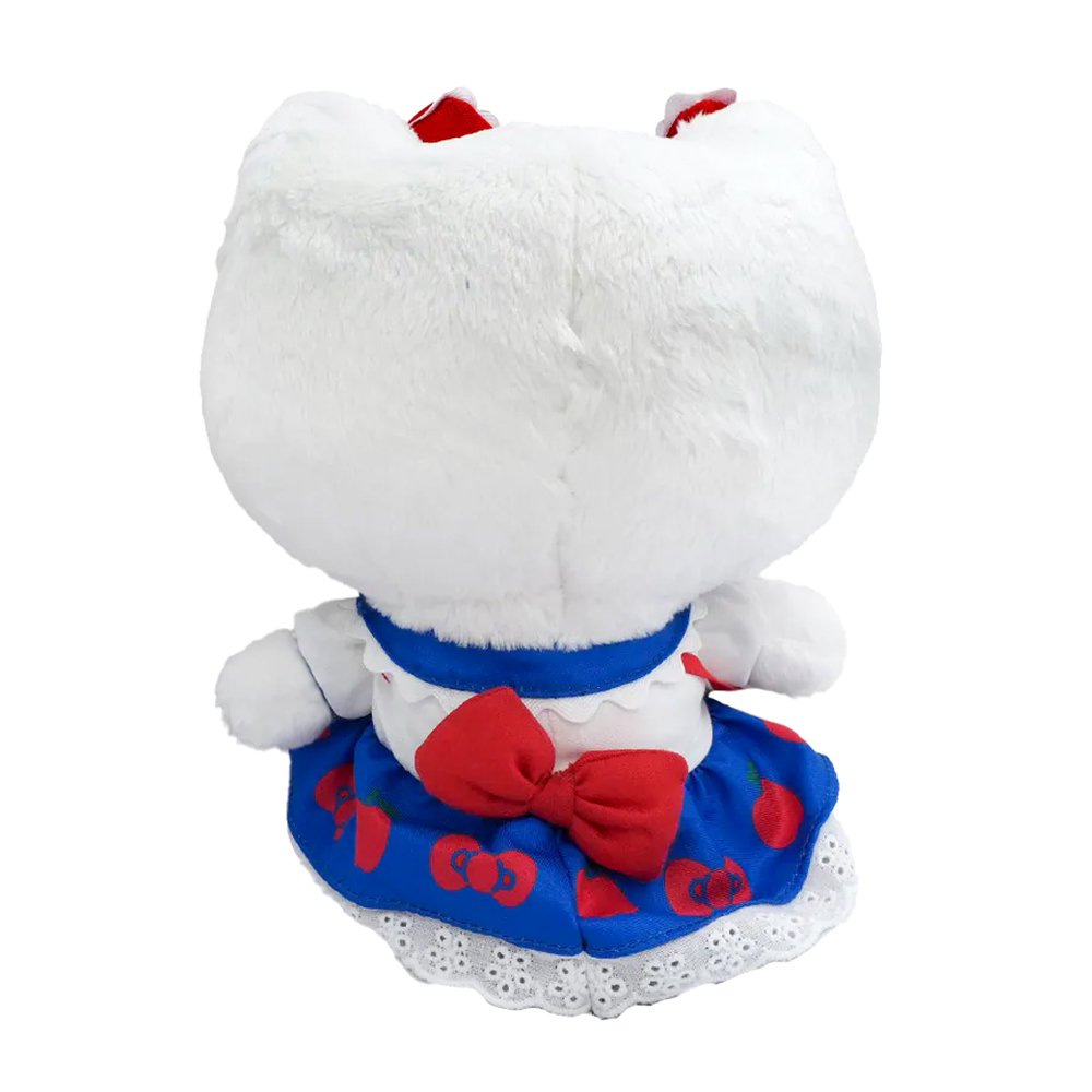 An officially licensed Hello Kitty plush wearing a blue apple-print skirt with a white lace hem, a white shirt with a blue collar, and a red crossbody bag. She has multiple red and blue bows on her head and is wearing red shoes.