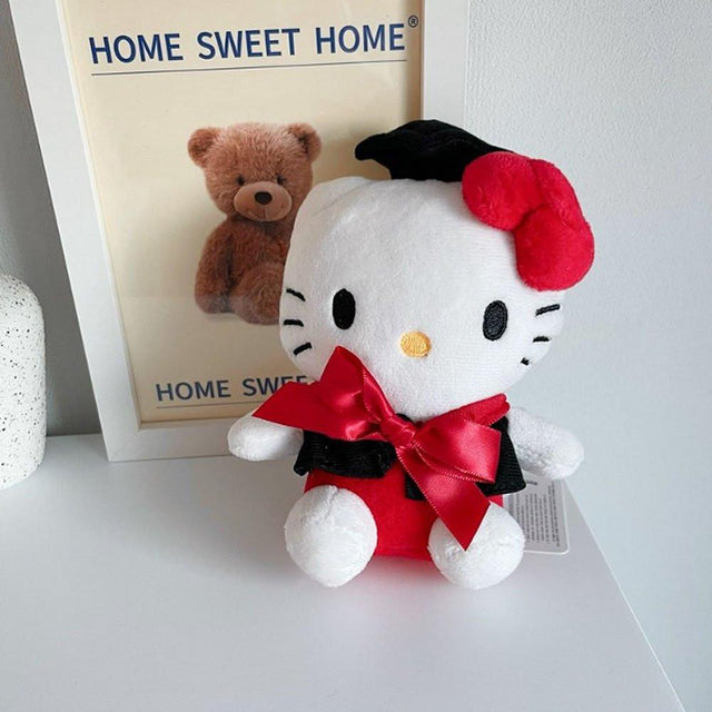 An officially licensed Sanrio Hello Kitty plush toy dressed in a black graduation cap with a gold tassel and a matching gown featuring a large red bow
