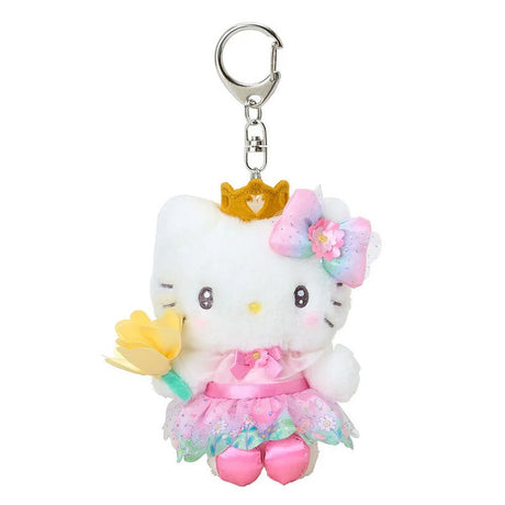 A plush keychain of Hello Kitty dressed as a princess. She wears a golden crown, a pink dress with a floral organza skirt, and a rainbow gradient bow with a pink flower. She is holding a yellow flower and has a silver metal keychain clip attached to her head.