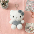 An officially licensed Sanrio Hello Kitty fluffy white plush keychain wearing a gray romper outfit and a matching gray bow