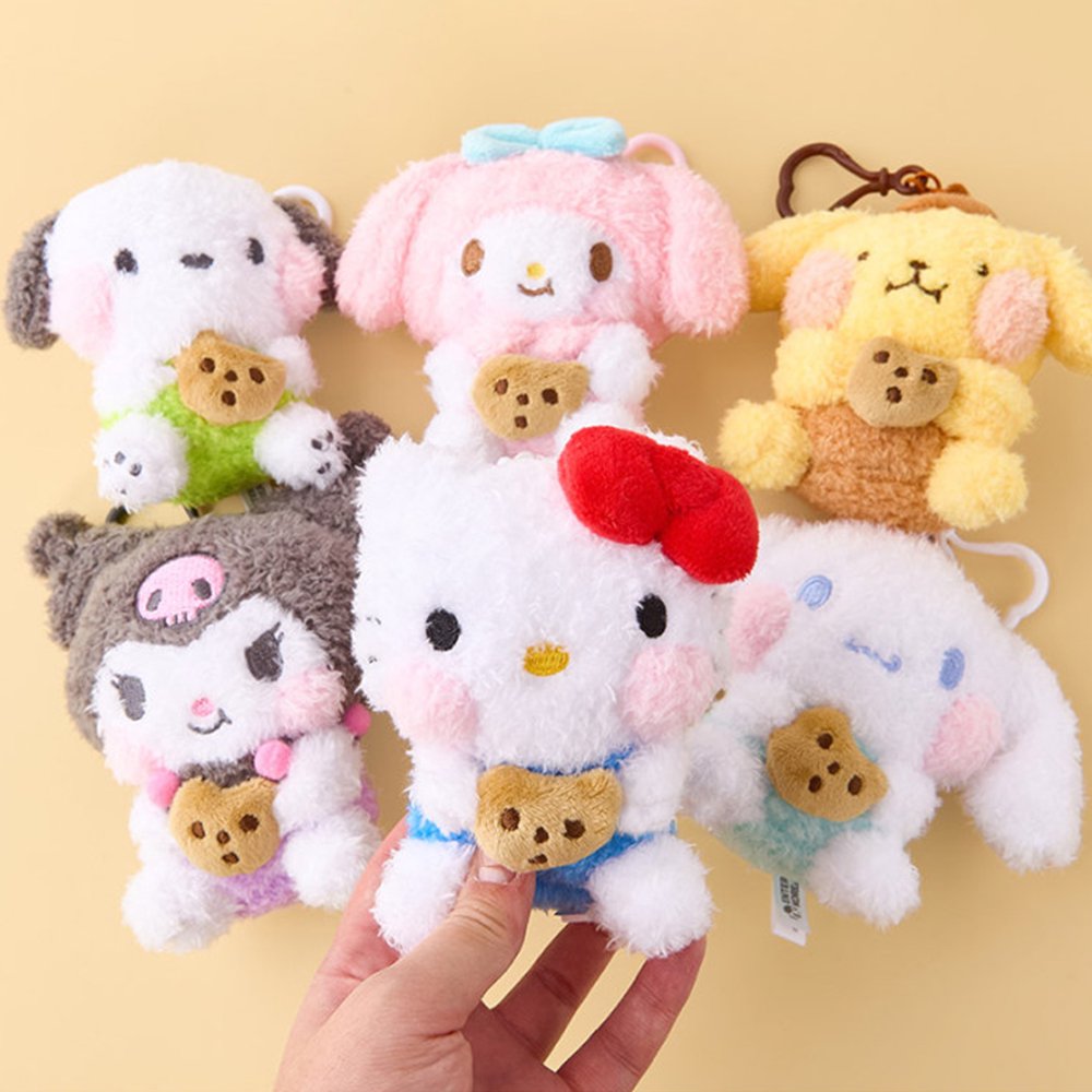 An officially licensed Sanrio collection of six shaggy-textured plush keychains including Hello Kitty, My Melody, Kuromi, Cinnamoroll, Pochacco, and Pompompurin, each holding a chocolate chip cookie. They are shown together with their respective heart-shaped clips.