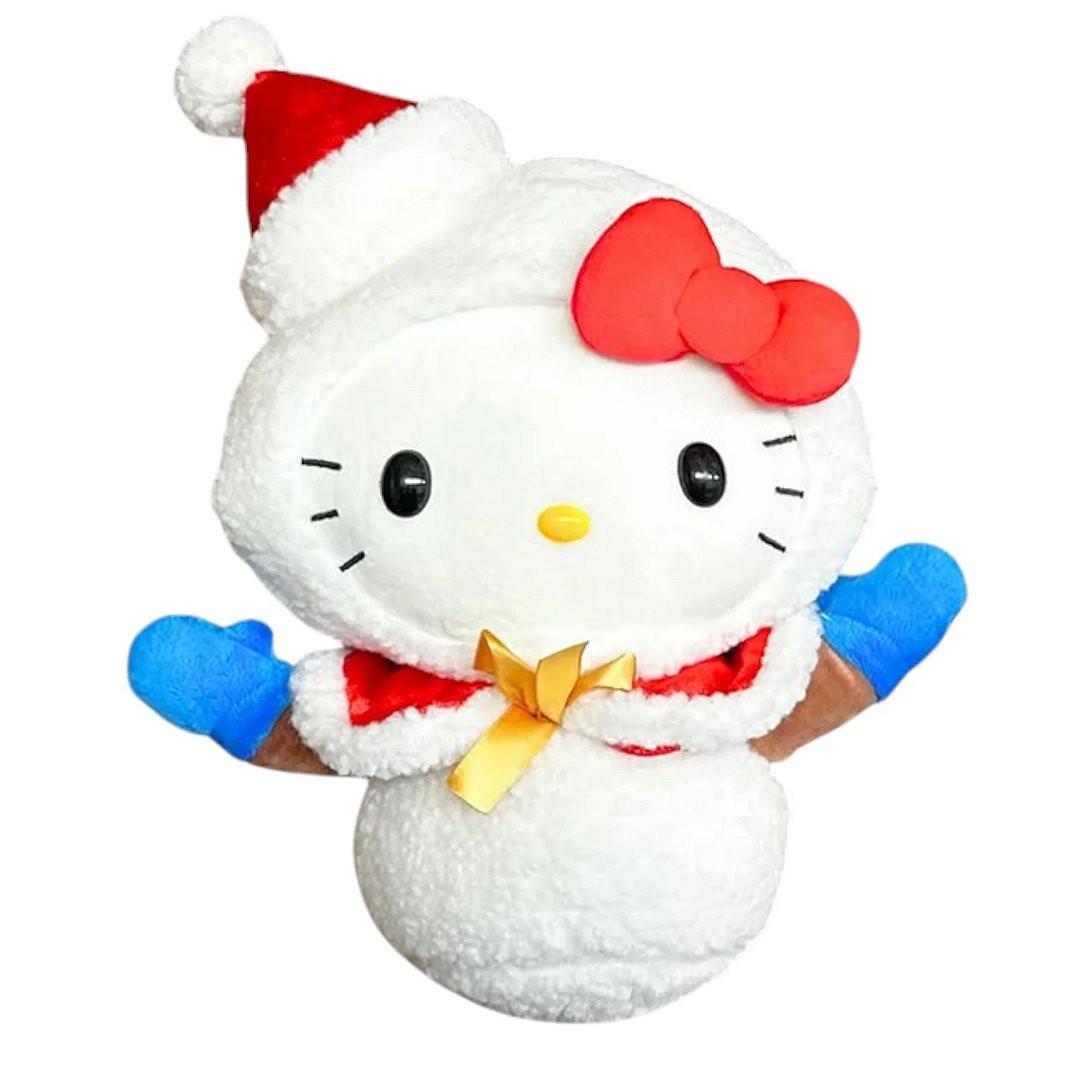 Hello Kitty Plush toy in a snow man costume with a red hat and cape with gold ribbon on a white background. She's perfect for Christmas decoration, displaying, bag decoration or gifting Christmas to Sanrio fans of all ages.