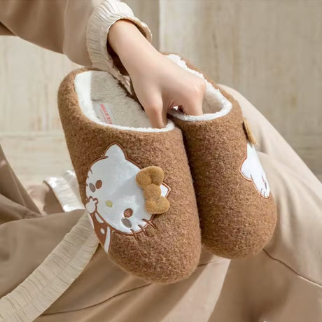 A pair of brown textured sherpa fleece Hello Kitty slippers with a white fleece interior, featuring a side-profile Hello Kitty embroidery with a 3D fuzzy brown bow.