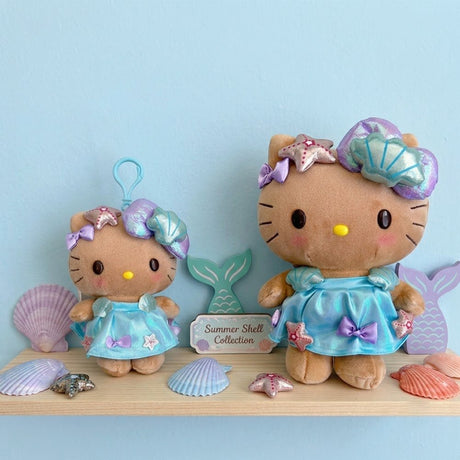 An officially licensed Sanrio collection of Hello Kitty plush toy and plush keychain with tan fur, dressed in a shimmering iridescent blue dress and an oversized metallic teal seashell headband.
