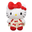 An officially licensed Hello Kitty plush doll wearing a cream-colored satin dress decorated with small red bows. She has a large red plush bow on her head and a second smaller red bow on her other ear.