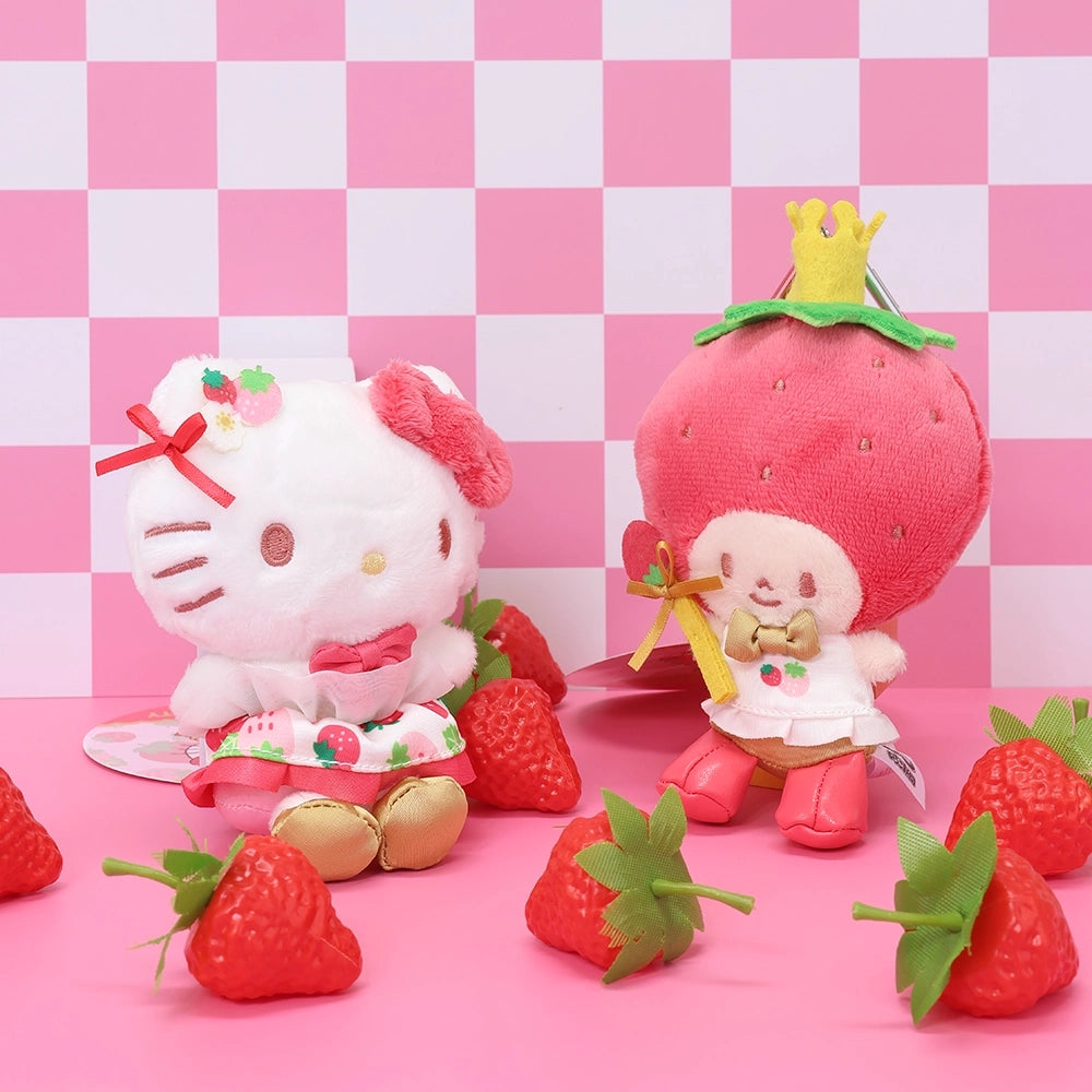 A promotional photo for the Sanrio Strawberry News 50th Anniversary Series featuring Hello Kitty and the Strawberry King plushies. Hello Kitty is sitting on the left in her strawberry print dress and gold shoes, while the Strawberry King stands on the right wearing a large strawberry headpiece with a gold crown. The scene is set against a pink and white checkered background with artificial strawberries scattered on a pink surface.