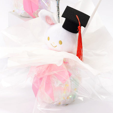 An officially licensed Class of 2026 Sanrio graduation gift set featuring six popular plush characters, Usahana, Corocorokuririn, Wish Me Mell, and Dinguri Days Mashu wearing black graduation caps. The characters are arranged like a bouquet with silver star balloons and "Congrats Grad" decorations.