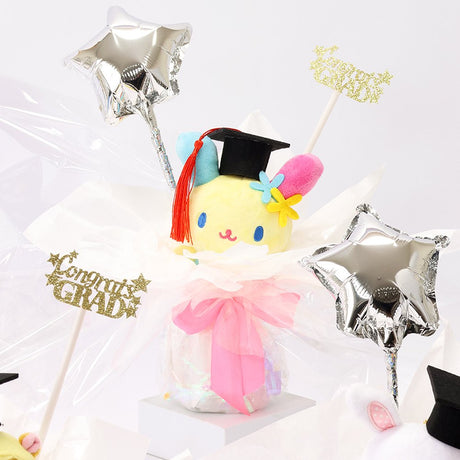 An officially licensed Class of 2026 Sanrio graduation gift set featuring six popular plush characters, Usahana, Corocorokuririn, Wish Me Mell, and Dinguri Days Mashu wearing black graduation caps. The characters are arranged like a bouquet with silver star balloons and "Congrats Grad" decorations.