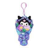 An officially licensed Sanrio Kuromi plush bouquet keychain featuring the character nestled among purple flowers, wrapped in shimmering iridescent blue fabric. The bouquet is accented with purple satin ribbons and a large, sparkling purple sequin bow at the base.