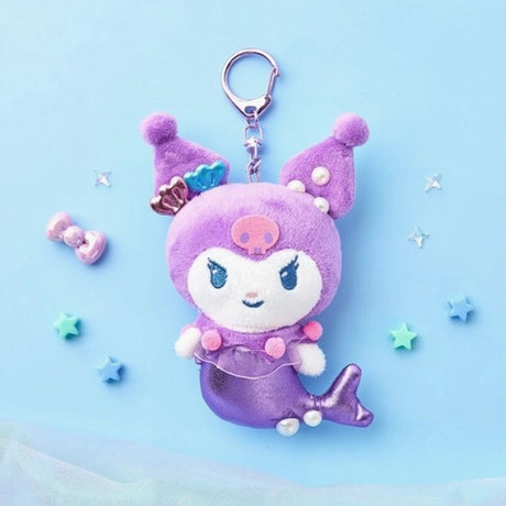 An officially licensed Sanrio character, Kuromi mermaid plush keychain featuring a metallic purple tail, a purple jester hood with a pink skull emblem, and small shell and pearl accessories. She has a sheer purple ruffle with pink pom-poms around her waist and a silver metal clip.