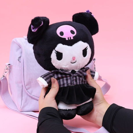 Officially licensed Sanrio Kuromi plush doll, held in hands, wearing a black and white plaid school uniform dress with a black velvet pleated skirt. Kuromi's signature pink skull is embroidered on her black head. The plush is displayed in front of a light purple cross-body bag.