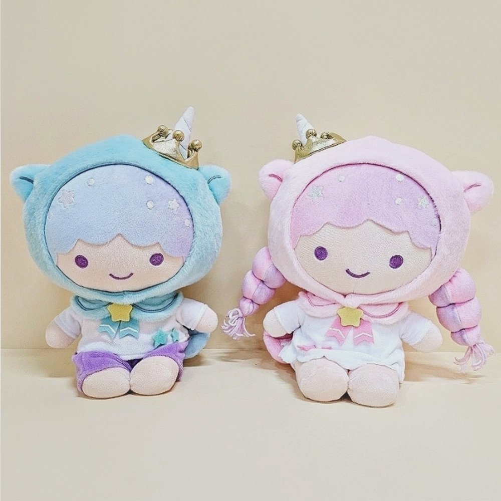 An officially lincensed Sanrio character plush set of the Little Twin Stars, Kiki and Lala, wearing unicorn-themed hoodies with gold crowns and horns. Kiki is on the left in a blue hood and purple shorts, while Lala is on the right in a pink hood with long braids and a white dress.