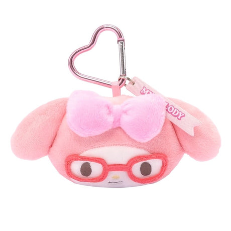 An officially licensed Sanrio My Melody plush head keychain, wearing embroidered red glasses and a textured pink bow. The keychain features a pink, heart-shaped metal carabiner clip and a woven fabric tag that reads "MY MELODY." The sturdy, heart-shaped carabiner in a matching metallic pink finish, makes it easy to clip onto backpacks, purses, or belt loops.