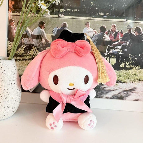 An officially licensed Sanrio My Melody plush toy dressed in a black graduation cap with a gold tassel and a matching gown featuring a large pink bow