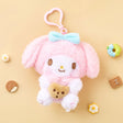 A high-texture, shaggy pink My Melody plush keychain holding a small brown chocolate chip cookie. She features a blue bow, rosy pink cheeks, and is attached to a pink heart-shaped plastic clip.