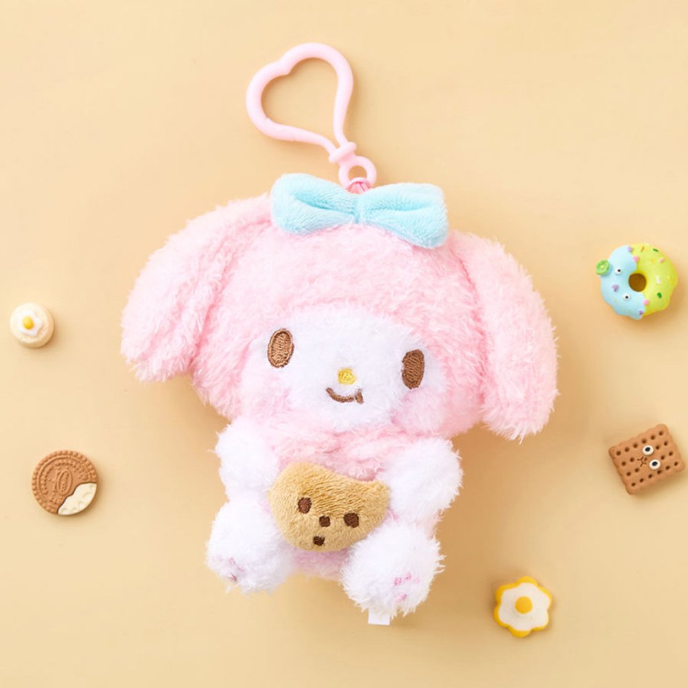 A high-texture, shaggy pink My Melody plush keychain holding a small brown chocolate chip cookie. She features a blue bow, rosy pink cheeks, and is attached to a pink heart-shaped plastic clip.