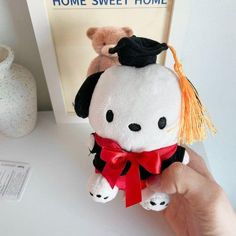 An officially licensed Sanrio Pochacco plush toy dressed in a black graduation cap with a gold tassel and a matching gown featuring a large red bow