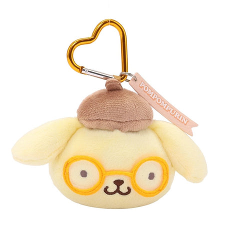 An officially licensed Sanrio Pompompurin plush head keychain, featuring his trademark brown beret and matching embroidered yellow glasses. The keychain features a yellow, heart-shaped metal carabiner clip and a woven fabric tag that reads "POMPOMPURIN." The sturdy, heart-shaped carabiner in a matching metallic yellow finish, makes it easy to clip onto backpacks, purses, or belt loops.