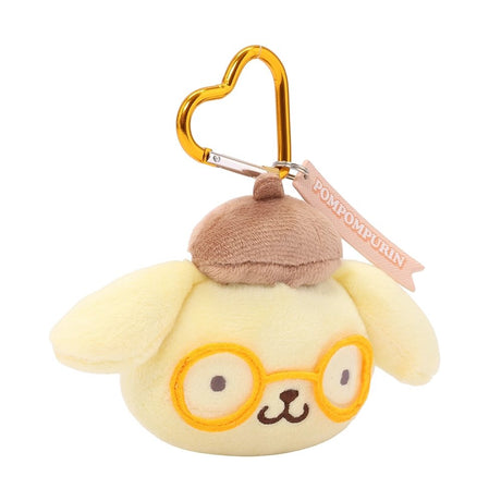 An officially licensed Sanrio Pompompurin plush head keychain, featuring his trademark brown beret and matching embroidered yellow glasses. The keychain features a yellow, heart-shaped metal carabiner clip and a woven fabric tag that reads "POMPOMPURIN." The sturdy, heart-shaped carabiner in a matching metallic yellow finish, makes it easy to clip onto backpacks, purses, or belt loops.