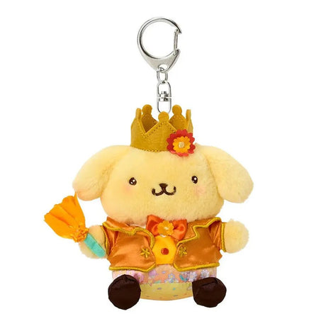 A plush keychain of the Sanrio character Pompompurin, a yellow golden retriever. He wears a golden crown with a red flower on his head, a shimmering orange-gold tuxedo jacket with gold trim, and a matching orange bowtie. He holds an orange flower in his hand and features a silver metal lobster clasp.