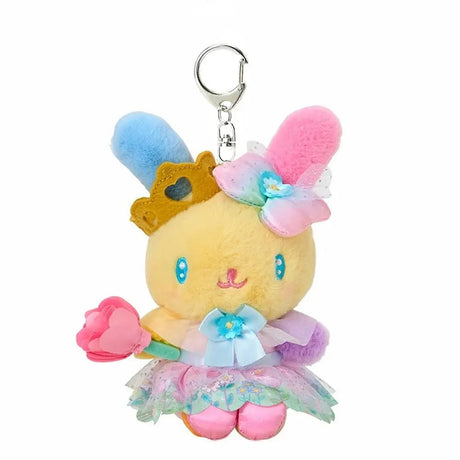 A plush keychain of the Sanrio bunny character Usahana. She has yellow fur with one blue ear and one pink ear. She wears a golden crown, a pastel rainbow gradient bow, and a pink princess dress with a floral organza overlay. She holds a pink flower and is attached to a silver metal lobster clasp.