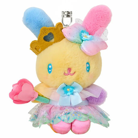 A plush keychain of the Sanrio bunny character Usahana. She has yellow fur with one blue ear and one pink ear. She wears a golden crown, a pastel rainbow gradient bow, and a pink princess dress with a floral organza overlay. She holds a pink flower and is attached to a silver metal lobster clasp.