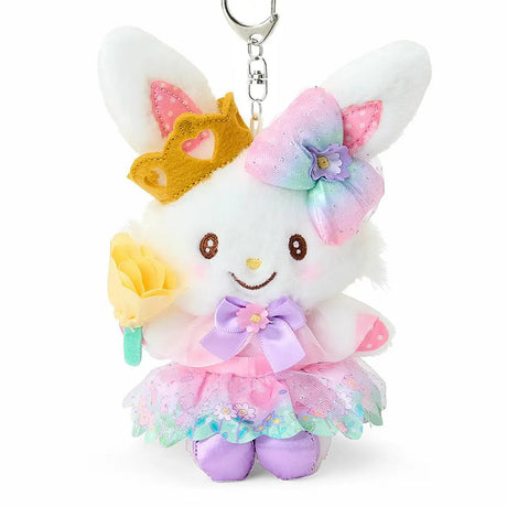 A plush keychain of the Sanrio character Wish me mell, a white bunny with pink-and-white polka dot patterns inside her ears. She is wearing a golden crown, a large rainbow-gradient bow, and a lavender-and-pink princess dress with a floral organza skirt. She holds a yellow flower and is attached to a silver metal lobster clasp.