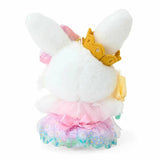 A plush keychain of the Sanrio character Wish me mell, a white bunny with pink-and-white polka dot patterns inside her ears. She is wearing a golden crown, a large rainbow-gradient bow, and a lavender-and-pink princess dress with a floral organza skirt. She holds a yellow flower and is attached to a silver metal lobster clasp.