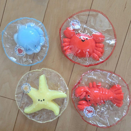 Seafood Mochi Squishy Toy Keychain Collection packaged in realistic mini market mesh, featuring a light blue octopus, red crab, yellow starfish, and orange lobster. These soft-textured mochi squeeze toys are perfect stress relief gifts, kawaii bag charms, and unique desk accessories for kids and adult collectors