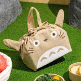 Officially licensed My Neighbor Totoro die-cut drawstring lunch pouch featuring 3D ears, Totoro's face, a drawstring tie, and top handles on natural beige fabric
