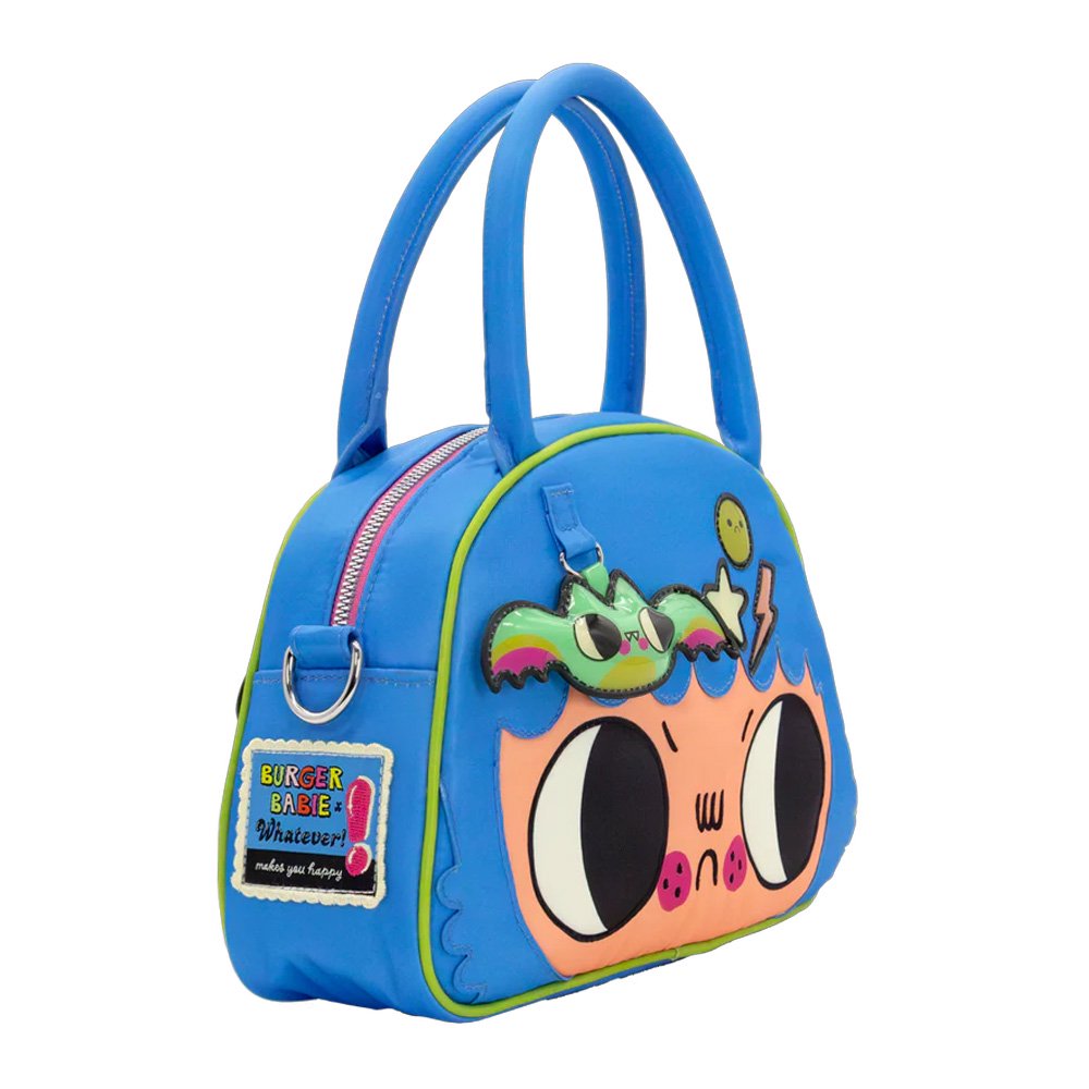 An officially licensed Whatever! blue dome-shaped handbag featuring a large character face with giant black eyes and pink cheeks. The bag is decorated with a green bat-winged patch, a star, and a lightning bolt. It includes blue top handles and a detachable rainbow-striped shoulder strap.