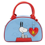 A light blue dome-shaped Snoopy crossbody bowler bag featuring Snoopy sitting on his red doghouse against a cloudy sky, with red handles, a striped rainbow shoulder strap, and a red heart-shaped Woodstock charm.