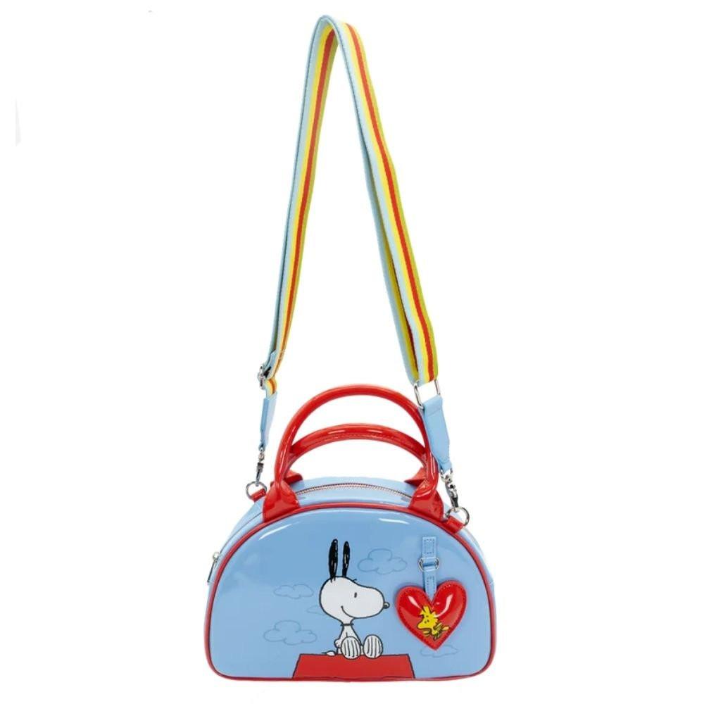 A light blue dome-shaped Snoopy crossbody bowler bag featuring Snoopy sitting on his red doghouse against a cloudy sky, with red handles, a striped rainbow shoulder strap, and a red heart-shaped Woodstock charm.