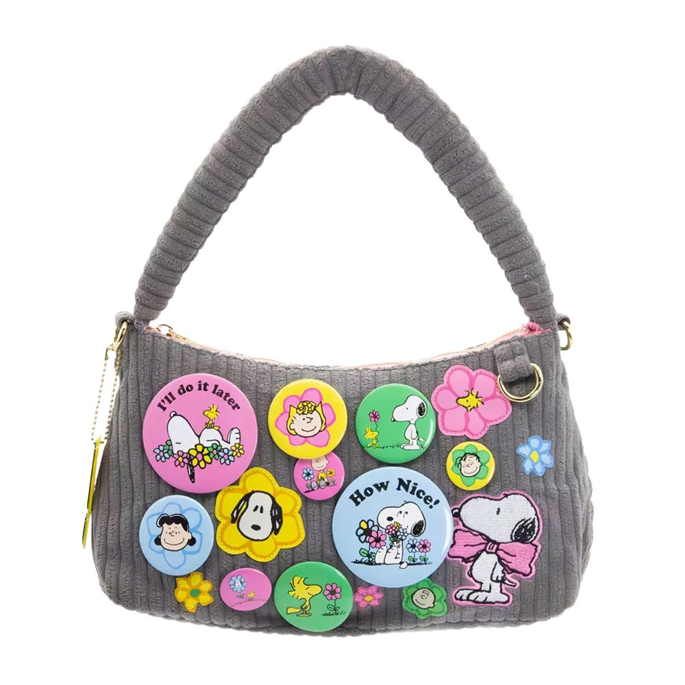 A grey corduroy shoulder bag decorated with an assortment of colorful Peanuts character buttons and floral patches