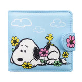 A light blue bi-fold wallet featuring Snoopy and Woodstock relaxing among colorful flowers, shown next to its open view displaying a bright yellow interior with card slots and a clear ID window.