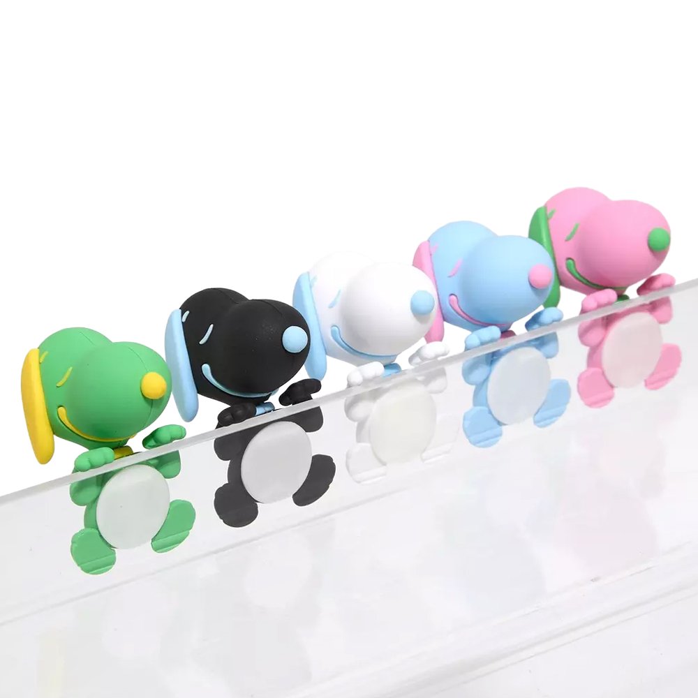 Five colorful miniature Snoopy figures in pastel sherbet colors designed to hang from edges, shown alongside a close-up of a blue and pink Snoopy figure clinging to the corner of a smartphone.

