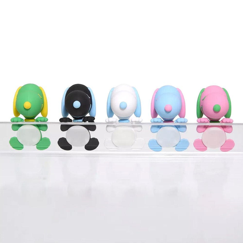Five colorful miniature Snoopy figures in pastel sherbet colors designed to hang from edges, shown alongside a close-up of a blue and pink Snoopy figure clinging to the corner of a smartphone.
