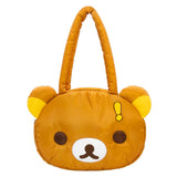 An officially licensed Rilakkuma puffy face crossbody bag in a brown color. It has a white muzzle with a brown nose and mouth, large dark eyes, and long padded shoulder straps. A small yellow exclamation point charm hangs from the base of one handle.