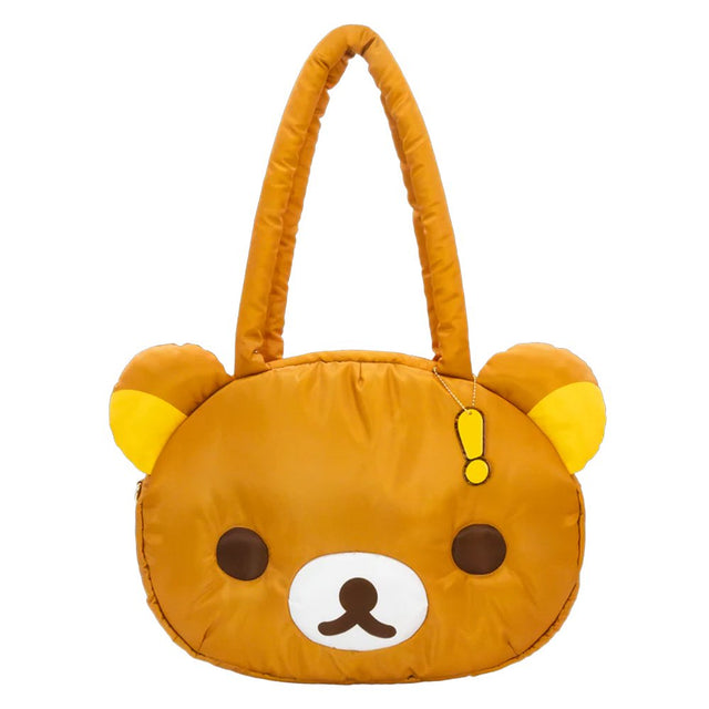 An officially licensed Rilakkuma puffy face crossbody bag in a brown color. It has a white muzzle with a brown nose and mouth, large dark eyes, and long padded shoulder straps. A small yellow exclamation point charm hangs from the base of one handle.