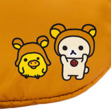 An officially licensed Rilakkuma puffy face crossbody bag in a brown color. It has a white muzzle with a brown nose and mouth, large dark eyes, and long padded shoulder straps. A small yellow exclamation point charm hangs from the base of one handle.