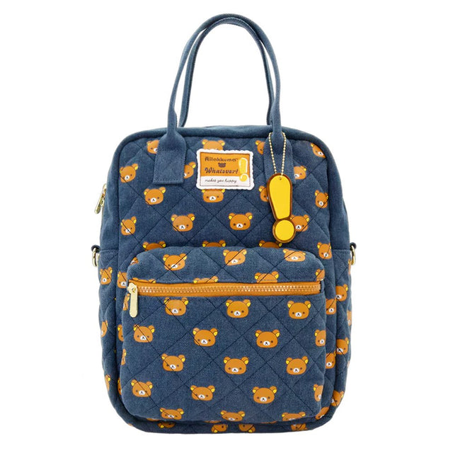 An officially licensed Rilakkuma reversible quilted backpack in navy denim blue. The front features a repeating pattern of Rilakkuma's face and a zippered front pocket.