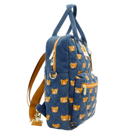 An officially licensed Rilakkuma reversible quilted backpack in navy denim blue. The front features a repeating pattern of Rilakkuma's face and a zippered front pocket.