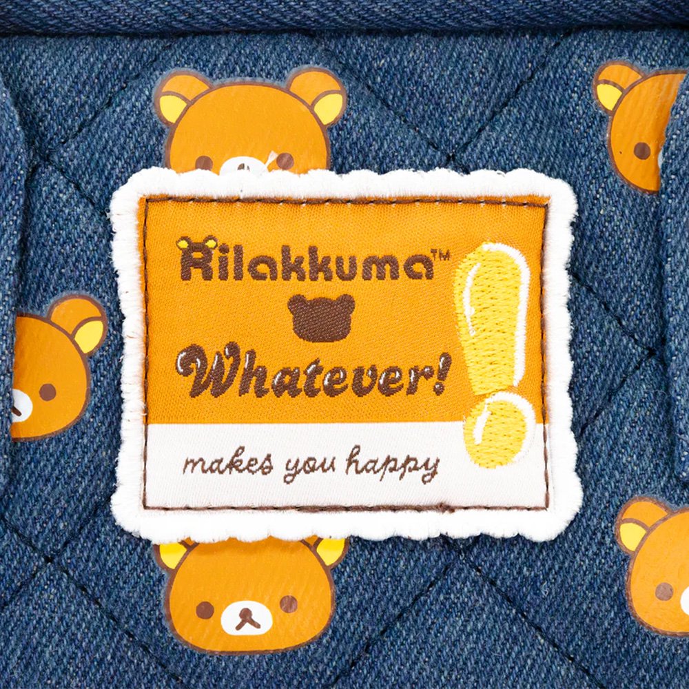 An officially licensed Rilakkuma reversible quilted backpack in navy denim blue. The front features a repeating pattern of Rilakkuma's face and a zippered front pocket.
