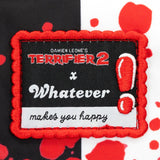 Reversible and convertible horror movie Terrifier 2 tote bag showcasing a split black-and-white design with red blood splatters, a bloody meat cleaver bag charm, and an Art the Clown charm